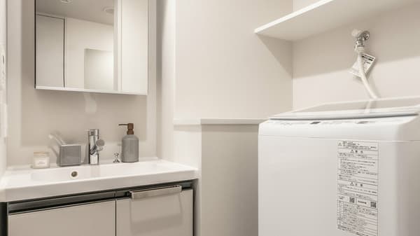 Modern vanity sink with a mirrored cabinet and a separate dedicated space for a white in-unit washing machine and storage shelf.