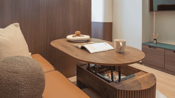 Close-up of a clever, lift-top wooden coffee table that transforms into a dining or workspace, set next to a brown leather sofa in the Premium Suite Queen living area.