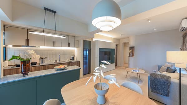 Wide shot of a contemporary open-plan living space with a kitchen featuring a green island, a light wood dining area, and a curved, built-in TV wall unit.