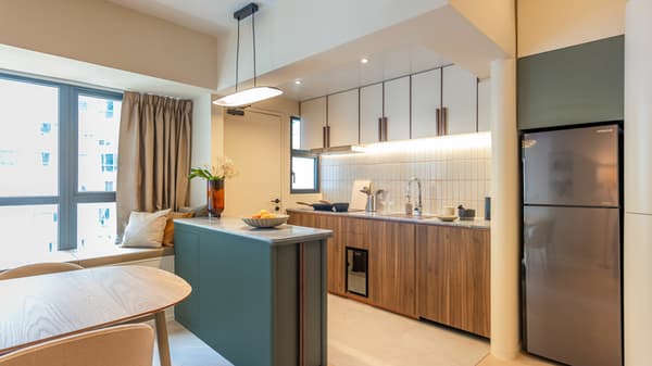 Modern apartment kitchen with a green island, wooden cabinets, a refrigerator, and a dining table next to a built-in window seat.