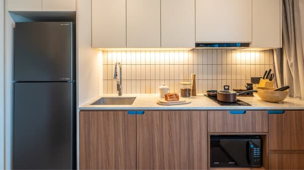 Compact kitchenette featuring wood lower cabinets, light upper cabinets, a dark integrated refrigerator, vertical beige backsplash tiles, and a built-in microwave.