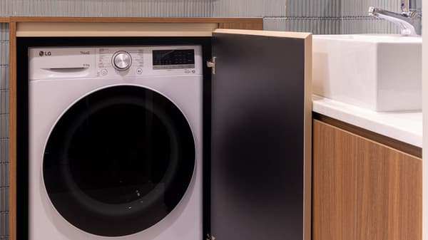 Close-up of a front-loading washer/dryer unit concealed behind a cabinet door in a modern bathroom area, next to a square sink.