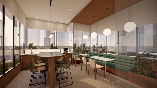 A bright, contemporary indoor resident lounge with floor-to-ceiling windows, featuring a high-top table with bar stools, a built-in green banquette, and a small kitchenette.