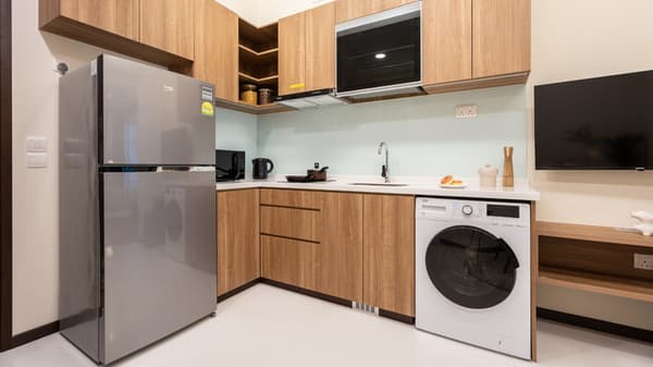L-shaped apartment kitchen featuring light wood cabinets, a full-sized silver refrigerator, and a washer/dryer unit integrated beneath the counter.