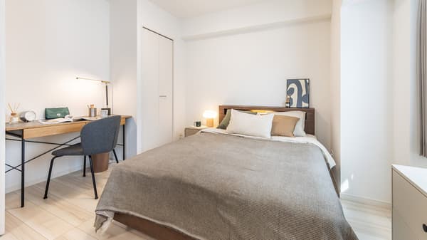 Bedroom featuring a double bed with neutral bedding and a dark wood headboard, next to a dedicated work area with a wooden desk and a chair.