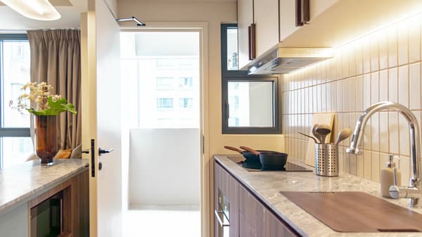 Close-up of a modern open kitchen with wood base cabinets, a marble countertop, an induction cooktop, and a doorway leading out to a small balcony area.