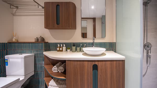 A contemporary bathroom featuring a white toilet and a curved wood-grain vanity with open shelving and a vessel sink. The wall is lined with a band of striking, dark blue vertical subway tiles.