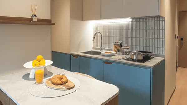 Stylish studio apartment kitchenette with bright blue lower cabinets, a light gray countertop, and a white tiled backsplash, featuring a sink and two-burner induction cooktop.
