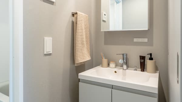 Bathroom vanity area featuring a square white sink set into a light gray cabinet, a mirrored wall cabinet above, and a beige towel hanging from a wall-mounted rail.