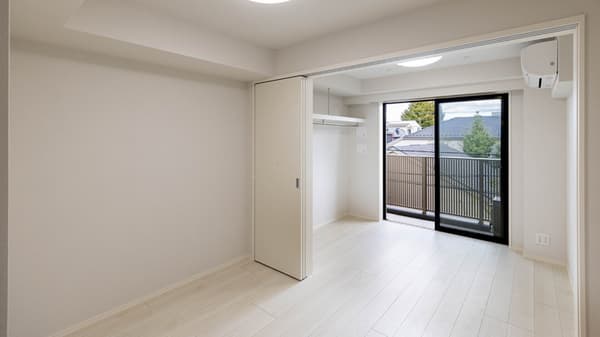 Unfurnished, brightly lit apartment room with light wood laminate flooring, a sliding closet door, and a large glass door leading to a balcony.