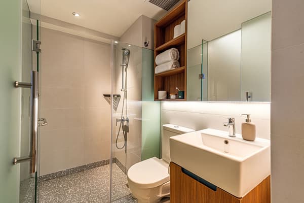 Modern bathroom in a premium suite featuring a square vessel sink on a wood-look vanity, a glass walk-in shower with gray terrazzo flooring, and wooden shelving above the toilet.