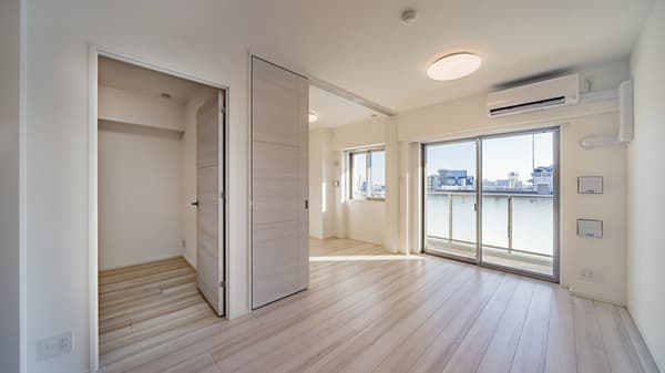 Bright living room with light wood-style flooring, a sliding glass door to a balcony, an air conditioner, and light wood sliding divider walls for an adjacent room.