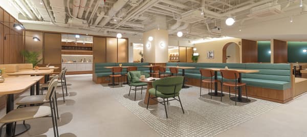 Stylish communal lounge and café space with mint green booth seating, modern wooden tables, contemporary chairs, and a visible communal kitchen area in the background.