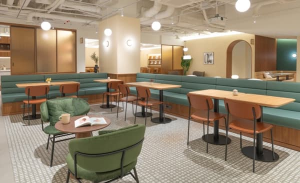 Vibrant communal dining area featuring long, upholstered green booth seating, small wooden tables, and casual accent chairs.