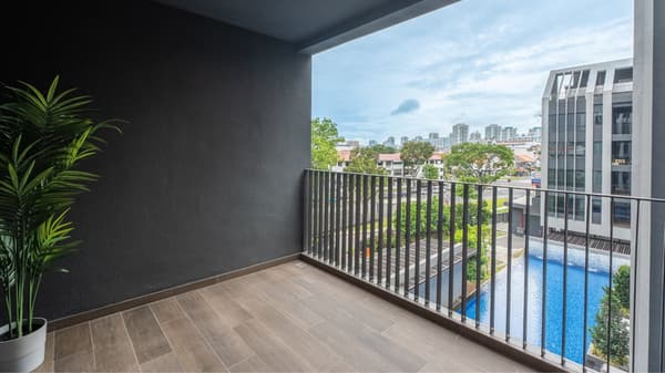Outdoor balcony with dark grey walls, wood-look tiled floor, and metal railing overlooking a swimming pool and a distant city skyline.