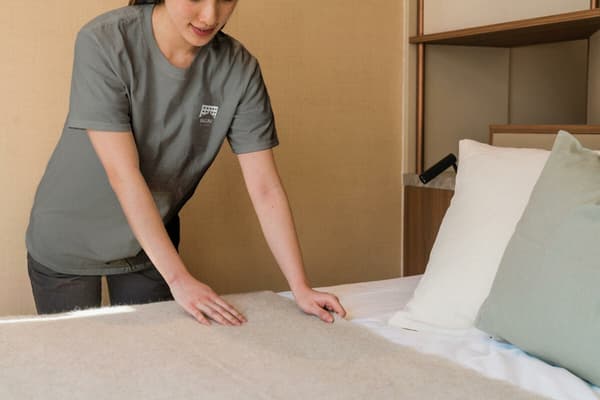 A person in a gray shirt carefully smoothing a neutral-colored wool throw blanket onto a freshly made bed.