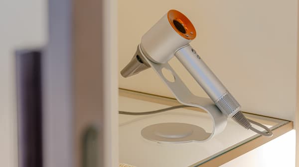 Close-up of a modern silver and orange Dyson Supersonic hair dryer displayed on its stand on a glass shelf in an apartment unit.