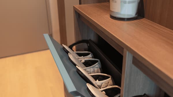 Close-up of a clever, space-saving pull-out shoe cabinet in a wood-finish entryway, with a pair of gray house slippers stored inside.