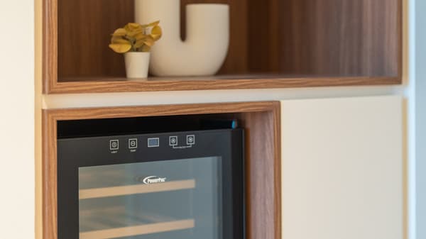 Close-up of a built-in wine cooler integrated into the cabinetry, surrounded by walnut wood shelving and a decorative vase.