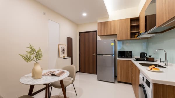 View of an apartment entrance area showing a dark wood door, a round marble dining table, and an adjacent kitchen with wood-look cabinets and a stainless steel refrigerator.