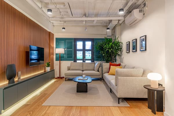 Comfortable resident lounge with a large sectional sofa, a wall-mounted TV above a gray console, and bright green window shutters.