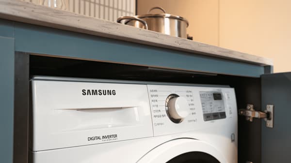 A close-up view of a compact, built-in Samsung digital inverter washer and dryer unit, integrated neatly below a kitchen countertop.
