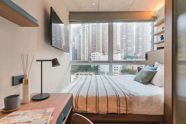 Modern Premium Suite bedroom at Weave Suites – Central West, featuring a queen bed with black and white stripes, a built-in desk, wall-mounted TV, and large windows with a city skyline view.