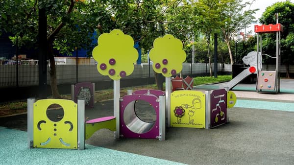 A bright and colorful children's playground area with tree-shaped cutouts, tunnels, a slide, and a rubberized safety floor.