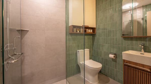 Modern bathroom with a glass-enclosed walk-in shower, toilet, vanity with wood paneling, and a sage green vertical subway tile accent wall.