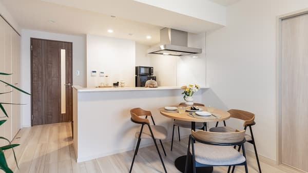View of the dining area in a large apartment, featuring a round wood table with four modern chairs and a white kitchen bar counter in the background.