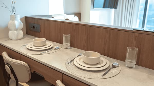 Close-up of a stylish two-person dining counter with contemporary place settings, round placemats, white textured bowls, and clear glasses, next to a decorative white vase.