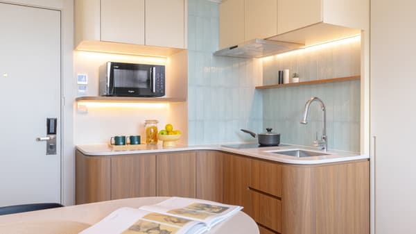 Modern compact kitchen with wood-grain base cabinets, white counters, a built-in sink and cooktop, a microwave on an open shelf, and light blue ridged tile backsplash.