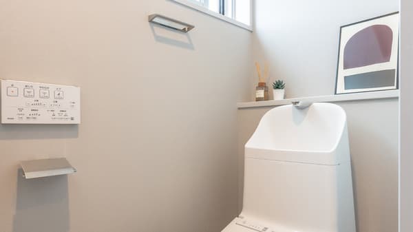 Close-up of a modern Japanese washlet toilet, showing the electronic control panel on the wall and a small window above the tank area.
