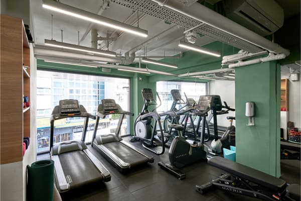 An on-site fitness center with bright green accent walls, featuring several treadmills, elliptical machines, and exposed ductwork on the ceiling.