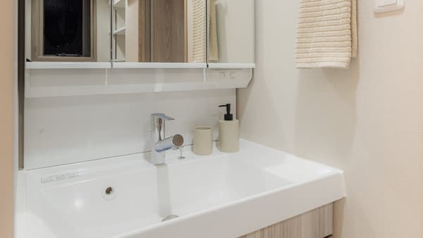 Bathroom vanity area with a white rectangular sink, modern faucet, mirrored medicine cabinet above, and light beige textured wallpaper in Monzennakacho.