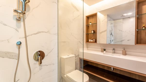 Modern bathroom featuring a glass-enclosed shower, a wall-mounted toilet, and a vanity with a large mirror and marble-patterned wall tiles.
