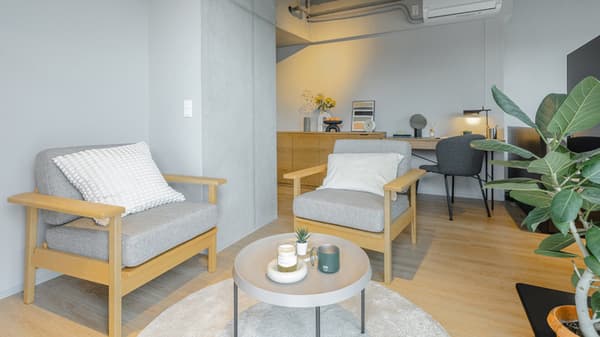 Close-up of the lounge area with two gray and wood armchairs, a white circular rug, and a light gray round coffee table with drinks and remote control.