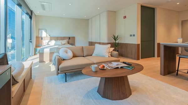A stylish view of the Junior Luxe Suite emphasizing the separation between the lounge area (sofa, coffee table) and the queen bed, with large wardrobe panels on the right and full-length windows on the left.