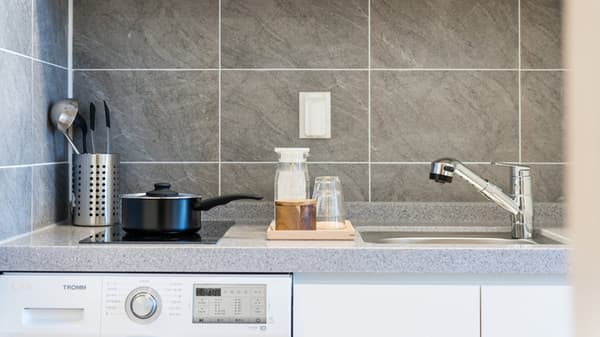 A compact kitchenette counter with a sink, induction cooktop, and a small pot, all above a front-loading washing machine.