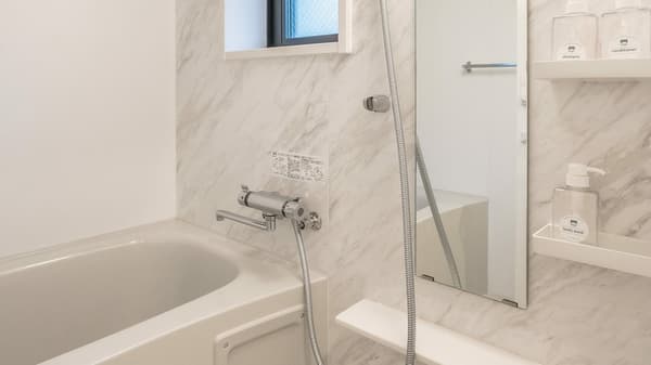 Clean bathroom with a deep white bathtub, shower hardware, and white marbled wall panels, featuring built-in shelving for toiletries.