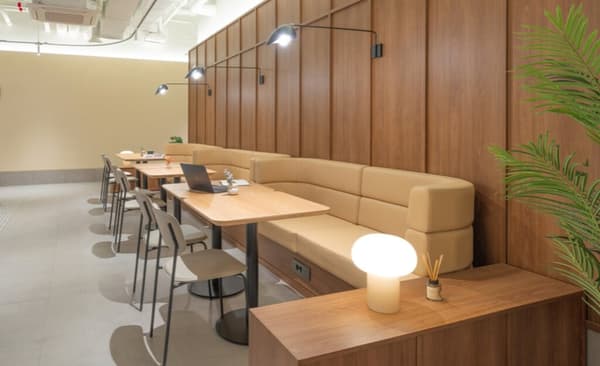 Focused working space with long, curved tan booth seating, individual desks, and warm wood paneling along the wall.