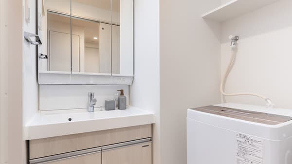 Modern bathroom vanity with a large mirrored cabinet and sink, next to an area containing an in-unit washing machine.