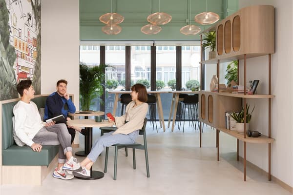 Bright, modern communal lounge area with a long wooden table, green accent wall, and residents sitting and talking in a stylish coliving space.