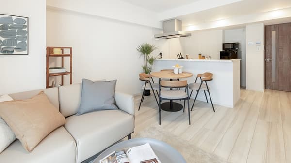 View from the living area toward the dining space, featuring a round wooden table with four modern chairs and a partial view of the minimalist kitchen counter.