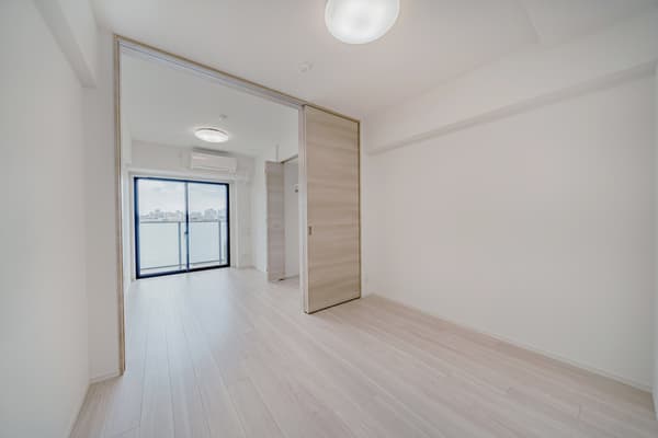 Living and dining room with light wood floors and white walls, featuring large sliding pocket doors that separate the main room from the bedroom with a balcony.