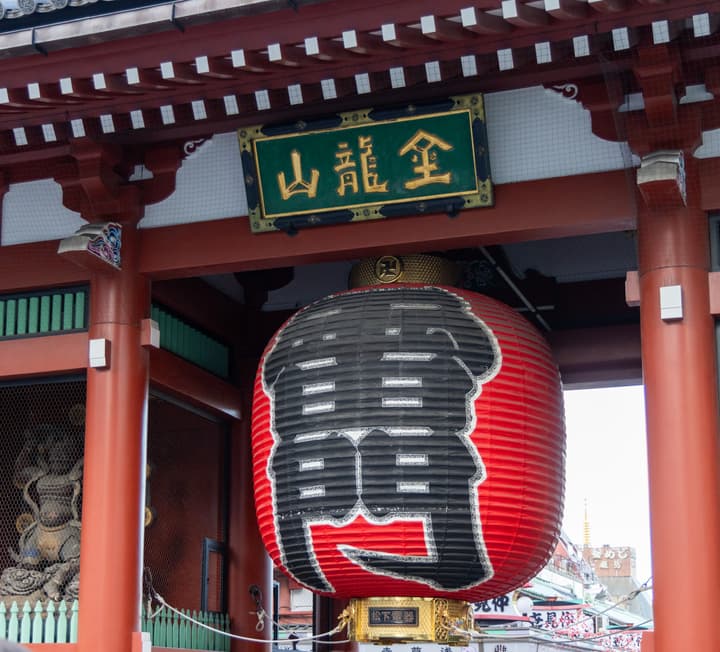 A close-up of the Kaminarimon (Thunder Gate) at Senso-ji Temple in Tokyo, featuring the iconic large red and black paper lantern and red wooden pillars.