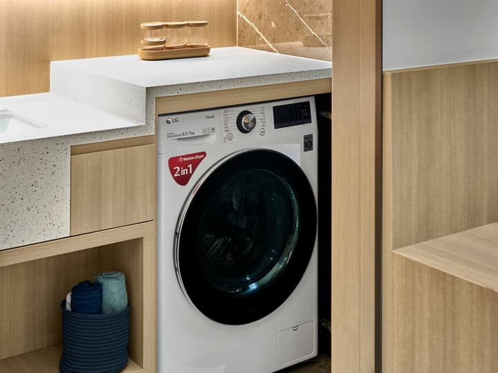 Compact laundry area in a modern apartment featuring an LG 2-in-1 washer dryer built into wooden cabinetry beneath a stone countertop.