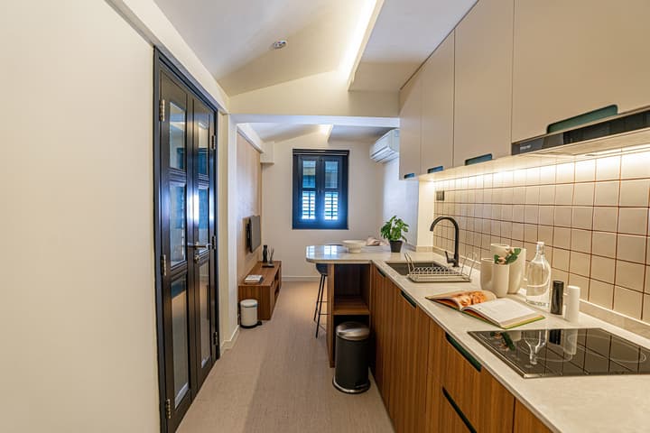 Compact, fully-equipped kitchenette and living area in a one-bedroom suite, featuring white and wood-look cabinets, an induction cooktop, and a small dining/bar counter.