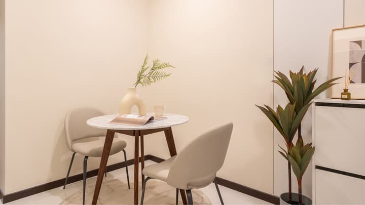 Close-up of a small dining nook with a round marble-top table, two beige chairs, and minimalist decor against a cream-colored wall.