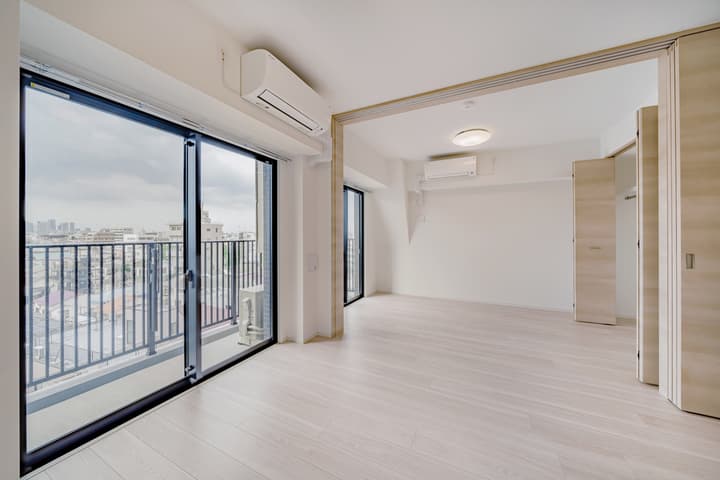 Spacious, unfurnished living and dining area with light wood floors, large sliding glass doors leading to a balcony, and a view of the city skyline.